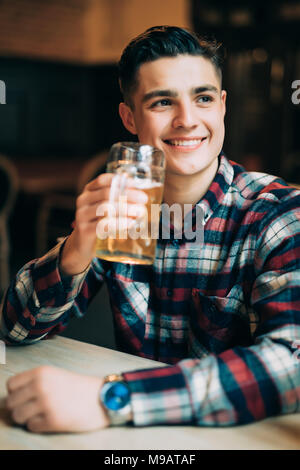 L'homme dans la bière pub. Cheerful young man holding a beer mug et smiling while sitting in bar Banque D'Images