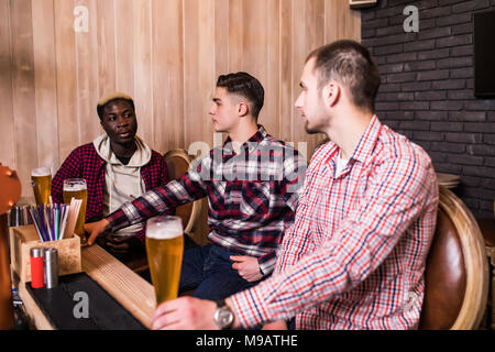 Les amis s'est réuni après une dure journée. Trois joyeux ami clink bière au bar et boire une bière. Banque D'Images