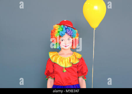 Bonheur clown girl posing près de yellow ballon d'air, à la caméra. Studio shot, isolé sur fond gris Banque D'Images