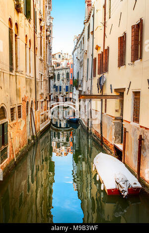 Backstreet étroit canal avec la réflexion du ciel dans l'eau, un petit pont et bâtiments colorés avec des fenêtres à volets, et bateaux Banque D'Images