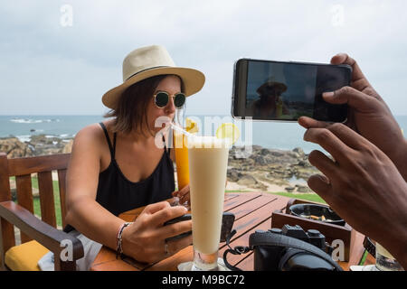 Jeune femme assise dans le boire du jus et d'attente pour les repas. Son mari en photo d'elle alors qu'elle ne le voit pas Banque D'Images