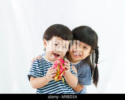 Little Boy holding fruit du dragon en main et belle fille stand up smiling sur fond blanc, asian girl type d'usure en tissu, Banque D'Images