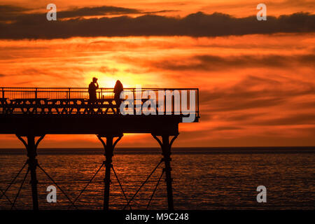 Pays de Galles Aberystwyth UK, samedi 24 mars 2018 Météo Royaume-uni : Les gens sont en silhouette debout sur la fin de la jetée de Aberystwyth au coucher du soleil spectaculaire sur la baie de Cardigan , à la veille de la période estivale, lorsque les horloges aller de l'avant et à l'heure ce soir Photo © Keith Morris / Alamy Live News Banque D'Images