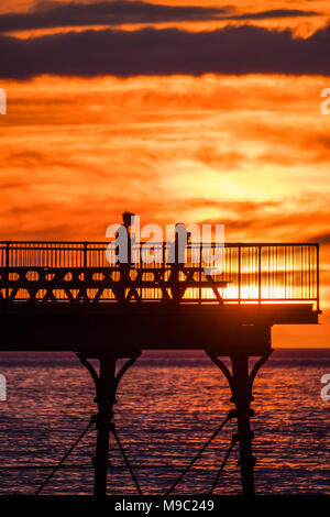 Pays de Galles Aberystwyth UK, samedi 24 mars 2018 Météo Royaume-uni : Les gens sont en silhouette debout sur la fin de la jetée de Aberystwyth au coucher du soleil spectaculaire sur la baie de Cardigan , à la veille de la période estivale, lorsque les horloges aller de l'avant et à l'heure ce soir Photo © Keith Morris / Alamy Live News Banque D'Images