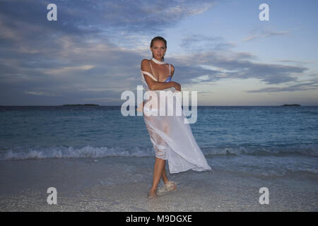 Young woman in bikini marche sur l'eau au coucher du soleil Banque D'Images