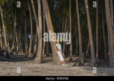 Belle Jeune femme debout dans une forêt tropicale s'appuyant sur un palmier Banque D'Images