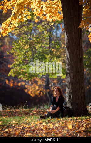 Femme mélancolique se repose sous un arbre. L'après-midi chaud émet une lumière à travers le feuillage d'automne, dans la région de Ringwood State Park, NJ Banque D'Images