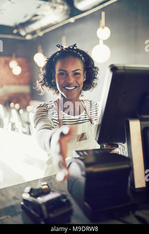 Smiling young African cafe owner standing à un terminal de point de vente dans son bistro l'extension d'une poignée Banque D'Images