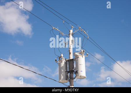 Deux transformateurs de puissance électrique sur un poteau avec les fils, les connecteurs et les isolants avec un ciel bleu profond et blanc fond de nuage. Banque D'Images