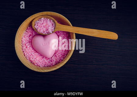 Concept de Spa et de bien-être - sel de mer rose dans le bol avec la cuillère en bois et le savon en forme de coeur mot amour sur fond de bois foncé sur elle. Spa Banque D'Images