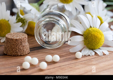 Une bouteille de globules homéopathiques avec fleurs de camomille dans l'arrière-plan Banque D'Images