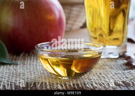 Le vinaigre de cidre de pomme dans un bol en verre, avec une pomme dans l'arrière-plan Banque D'Images