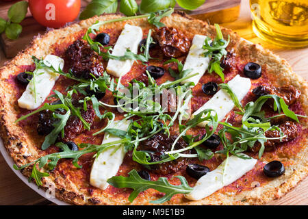 Pizza végétarienne sans gluten à base de chou-fleur et la farine d'amande, garnie de tomates séchées, olives, fromage de chèvre et roquette fraîche. Banque D'Images