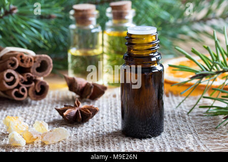 Une bouteille d'huile essentielle avec l'anis étoilé, cannelle, encens résine, tranche d'orange séchée, et les branches de pin et de sapin dans l'arrière-plan Banque D'Images