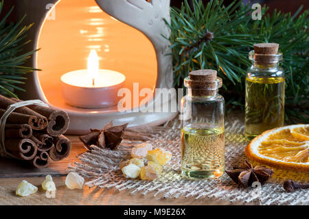 Sélection d'huiles essentielles à la badiane, girofle, cannelle, encens résine, tranche d'orange séchée, une lampe d'arome et branches de pins dans la ba Banque D'Images