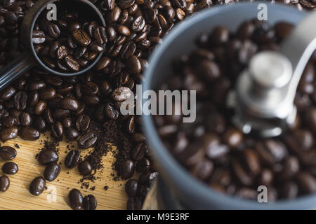 Moulin à café manuel et cuillère de mesure avec les grains de café renversé sur planche de bois. Banque D'Images