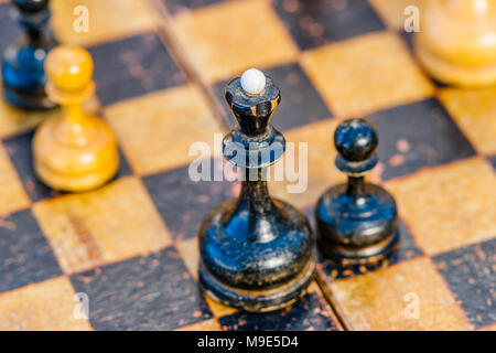 Vieux, utilisé, essuyé des échecs noir reine et un pion sur un échiquier. Se concentrer sur un grand chef, de pions blancs est visible Banque D'Images