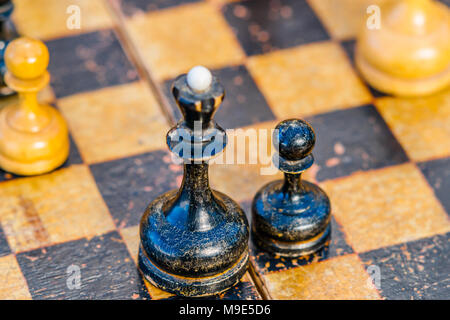 Vieux, utilisé, essuyé des échecs noir reine et un pion sur un échiquier. Se concentrer sur un pion, de pions blancs est visible Banque D'Images