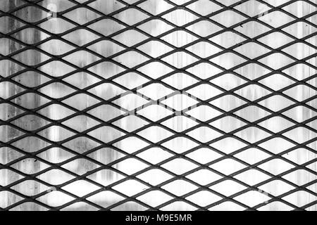 Dark metal wire mesh ou diagonale de protection souple, fond gris. Photo en noir et blanc Banque D'Images