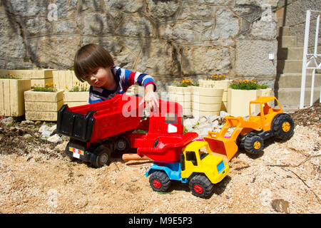 Petit garçon de trois ans jouant dans le sable avec une pelle et camion. Banque D'Images