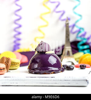 Gâteau rond lilas avec des macarons sur une planche de bois blanc, derrière un papier multicolores et serpentine une tour, Close up Banque D'Images