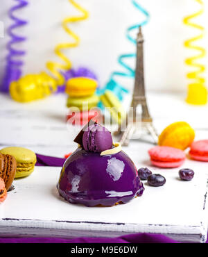 Gâteau rond lilas avec des macarons sur une planche de bois blanc, derrière une serpentine de papier multicolores Banque D'Images