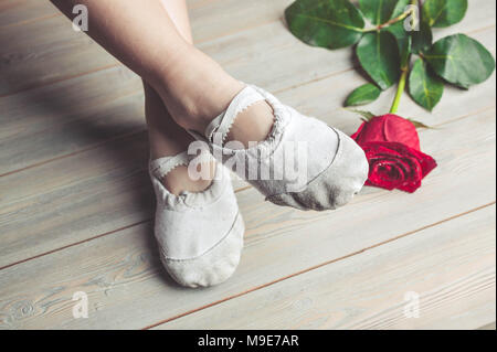 Une petite danseuse et une rose rouge. Les jambes d'une fille en chaussons de ballet sur un sol en bois Banque D'Images