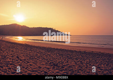 Coucher du soleil et de la mer. L'Inde Gokarna. Le soleil se couche sur la colline sur la mer. Le sable chaud jaune au premier plan. Banque D'Images