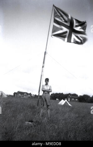 1934, historique, un jeune scout dans les champs à un camp scout à Dublin, Irlande, se dresse à côté de poudly de hauteur mât tenant une Union Jack flag/ Banque D'Images