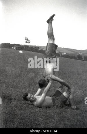 1934, historiques, deux garçons faisant des exercices ensemble - l'un faisant s'atr pris en charge par les autres- dans un champ à un camp scout, en Irlande. Lord Baden-Powell, fondateur du mouvement scout croyait en la devise, ''un corps sain, un esprit sain" et avait ceci à dire,''un pas vers le bonheur est de faire vous-même sain et fort bien que vous êtes un garçon, de sorte que vous pouvez être utile et ainsi vous pouvez profiter de la vie quand vous êtes un homme". Banque D'Images