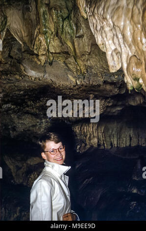 Jeune femme souriante portant des lunettes à cheveux courts dans une grotte sombre avec des stalactites, État de Washington États-Unis dans les années 1950 Banque D'Images