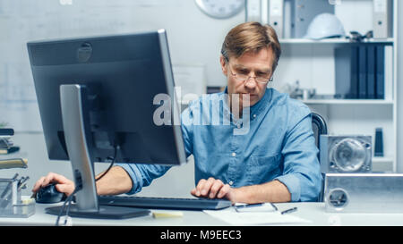 Bureau d'ingénierie d'occupation. Ingénieur en chef à son bureau de travail, certains éléments techniques se trouvant sur son bureau. Son assistant travaille à son bureau. Banque D'Images