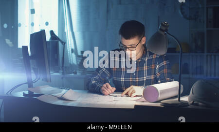 Jeune ingénieur civil architecte capable travailler tard Heures dans son bureau. Office est sombre seulement sa Table s'allume. Divers plans et devis Banque D'Images