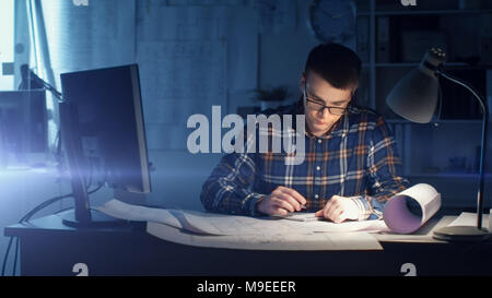 Jeune ingénieur civil architecte capable de travailler de nuit dans son bureau. Office est sombre seulement sa Table s'allume. Divers plans et devis Banque D'Images