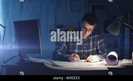 Jeune ingénieur civil architecte capable travailler tard Heures dans son bureau. Office est sombre seulement sa Table s'allume. Divers plans et devis Banque D'Images