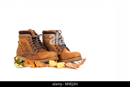 Une paire de daim élégant et élégant en cuir nubuck brun mans automne ou hiver boots avec des feuilles d'automne devant eux isolé sur blanc. Banque D'Images