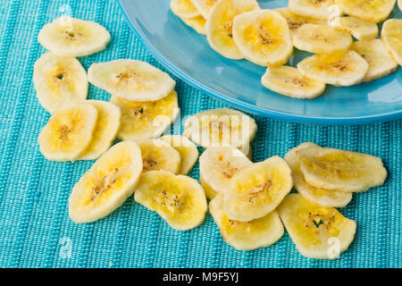 Tas de chips de banane séchée snack sur plaque bleue turquoise et le tapis sur la table Banque D'Images