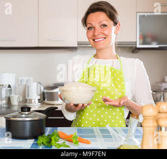 Happy smiling woman in apron cuisson du riz à la cuisine maison Banque D'Images