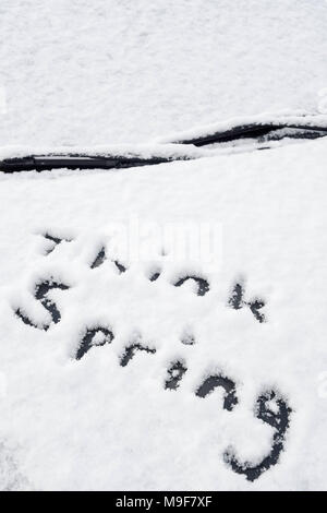 Le message 'pense que spring' écrit dans la neige fraîche sur un capot de voiture après une chute de neige en début de saison. Banque D'Images