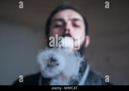 Homme avec Barbe et Mustages Vaping une cigarette électronique. Vaper fumée Hipster vaporisateur et Exhals des ronds de fumée. Banque D'Images