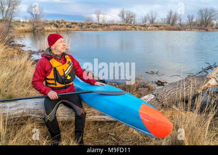 Senior male pagayeur repose sur une rive du lac après entraînement sur sa course stand up paddleboard, début du printemps paysage du Colorado Banque D'Images