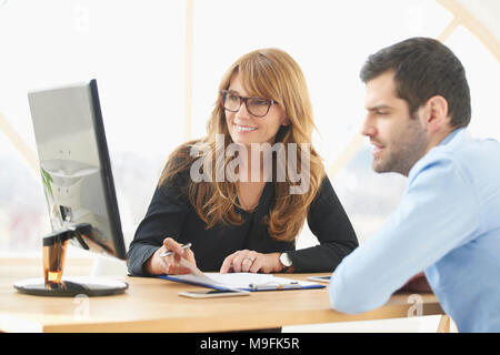Âge moyen exécutif businesswoman sitting at desk in front of laptop et faire quelques formalités administratives tout en donnant des conseils de vente à son jeune assistant. Brai Banque D'Images