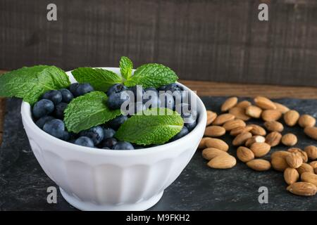 Prêt pour les fruits d'été ? Matières, sweet bleuets dans un bol blanc belle et le goût encore mieux. Le Citron et menthe ajouter un contraste lumineux de couleur. Banque D'Images