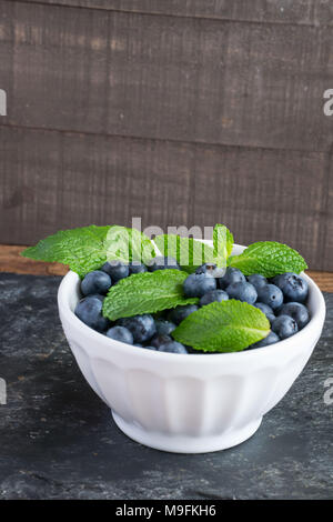 Prêt pour les fruits d'été ? Matières, sweet bleuets dans un bol blanc belle et le goût encore mieux. Le Citron et menthe ajouter un contraste lumineux de couleur. Banque D'Images