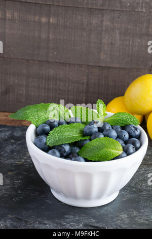 Prêt pour les fruits d'été ? Matières, sweet bleuets dans un bol blanc belle et le goût encore mieux. Le Citron et menthe ajouter un contraste lumineux de couleur. Banque D'Images