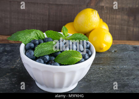 Prêt pour les fruits d'été ? Matières, sweet bleuets dans un bol blanc belle et le goût encore mieux. Le Citron et menthe ajouter un contraste lumineux de couleur. Banque D'Images