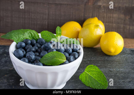 Prêt pour les fruits d'été ? Matières, sweet bleuets dans un bol blanc belle et le goût encore mieux. Le Citron et menthe ajouter un contraste lumineux de couleur. Banque D'Images