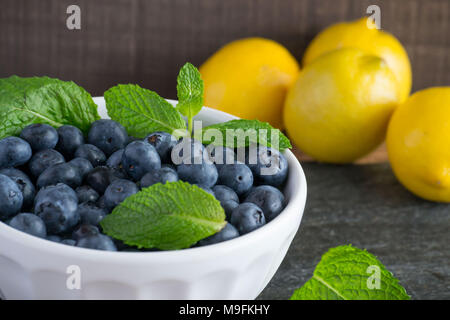 Prêt pour les fruits d'été ? Matières, sweet bleuets dans un bol blanc belle et le goût encore mieux. Le Citron et menthe ajouter un contraste lumineux de couleur. Banque D'Images