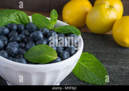 Prêt pour les fruits d'été ? Matières, sweet bleuets dans un bol blanc belle et le goût encore mieux. Le Citron et menthe ajouter un contraste lumineux de couleur. Banque D'Images