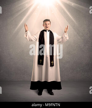 Un jeune prêtre religieux masculins en noir et blanc robe donnant sa bénédiction, tenant la sainte bible tout en étant éclairée par des rayons lumineux venant de concept ci-dessus Banque D'Images